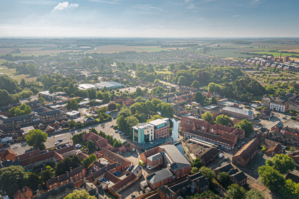 Aerial view of a small town with clustered buildings, roads, trees, and surrounding green fields under a clear blue sky.