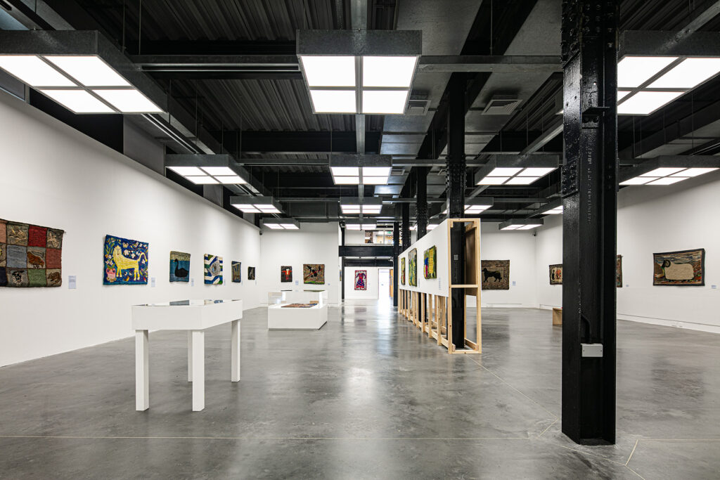 A modern art gallery with polished concrete floors, white walls, and various colourful paintings hung around the space and displayed on white tables.