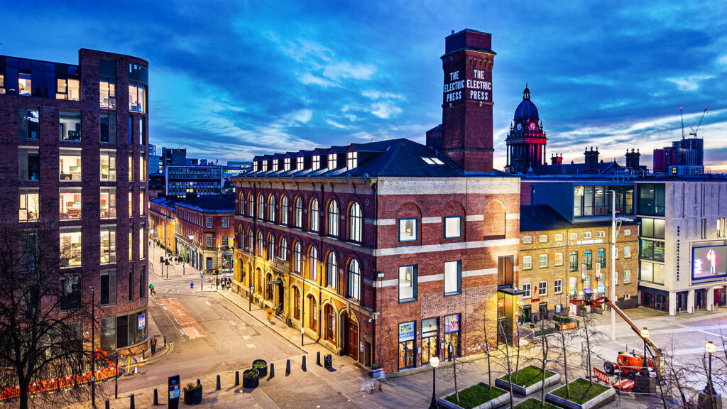 Evening view of The Electric Press building in a cityscape with modern and historic architecture under a blue, cloudy sky.