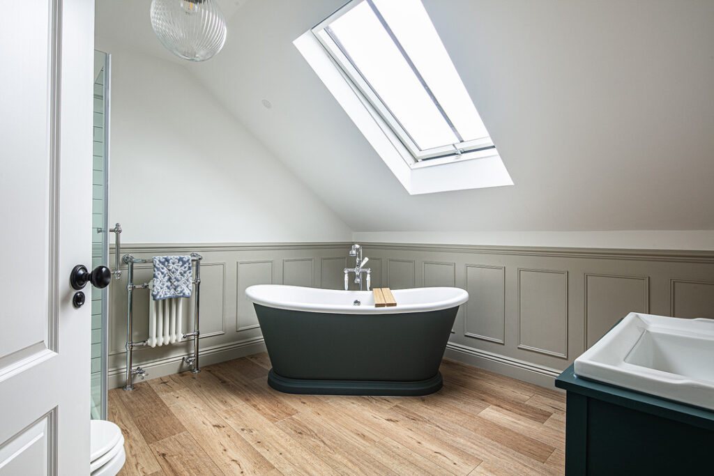 Modern attic bathroom with a skylight, freestanding bath, wooden floor, panelled walls, a towel rail, and a partial view of a shower and vanity unit.