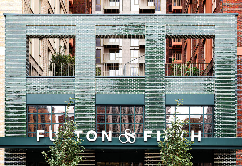 The exterior of a brick building with large green tiles, open windows, and a sign that reads Fulton & Finch.