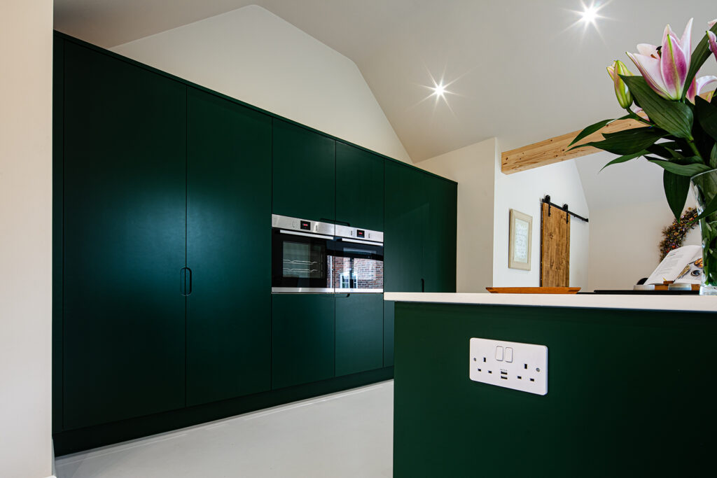 A kitchen with green cupboards and a white worktop.