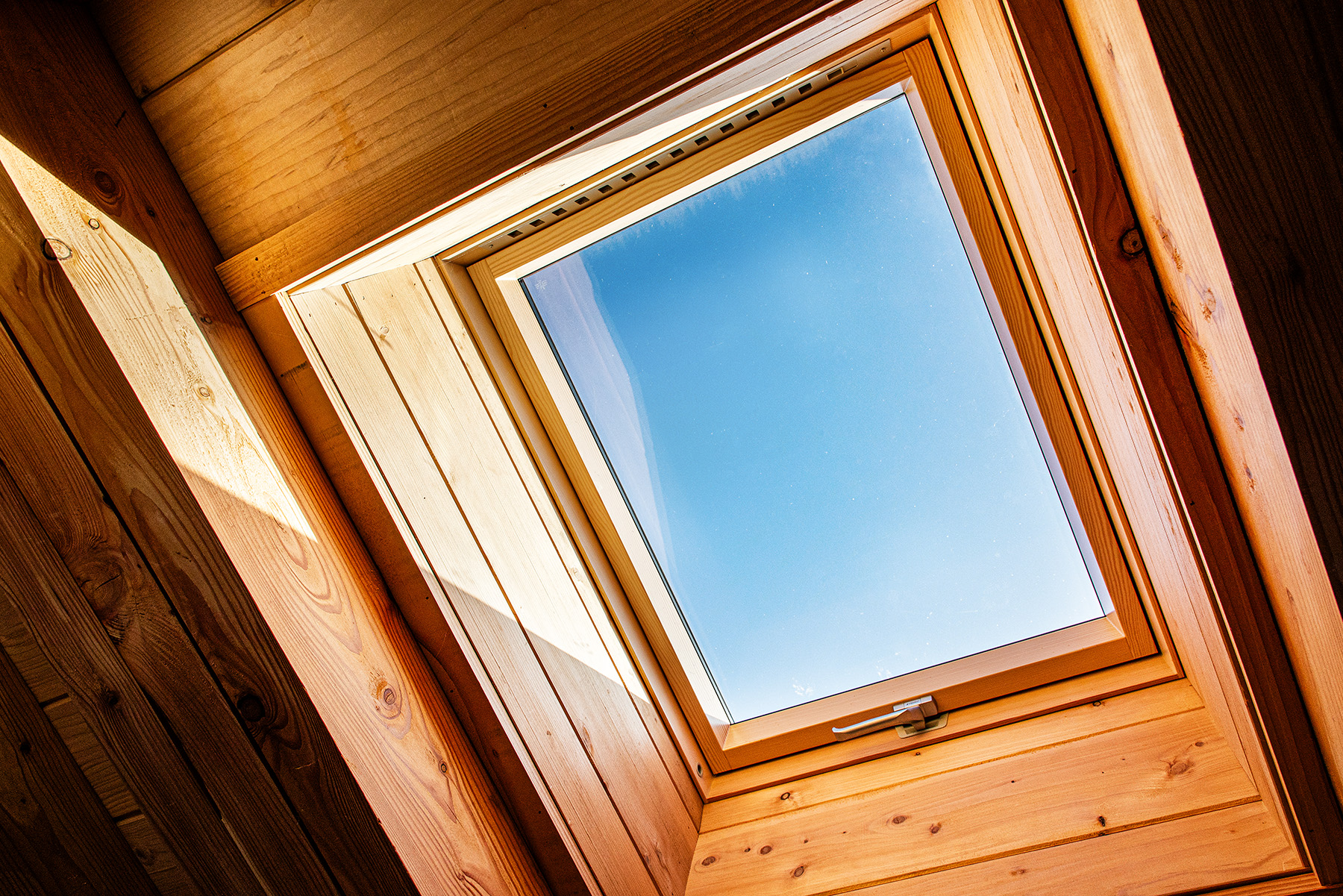 A rooflight window set in a wooden ceiling lets natural light into the room, showing a clear blue sky outside.