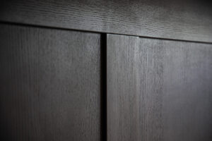 Close-up of two dark wooden panels with a vertical seam, showing the wood grain texture and a slight gap between the panels.