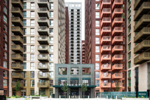 Tall modern apartment blocks with balconies surround the entrance to a building labelled Fulton & Fifth, with trees and signage in front.